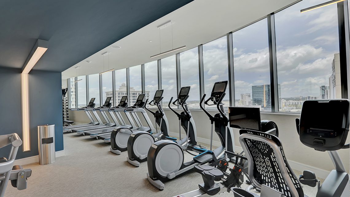 exercise equipment lined up against the windows of the gym