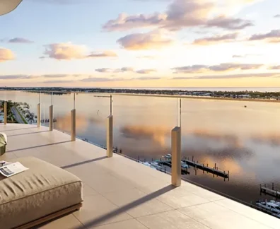 Penthouse terrace with lounge seating and glass railing overlooking a calm waterfront marina at sunset