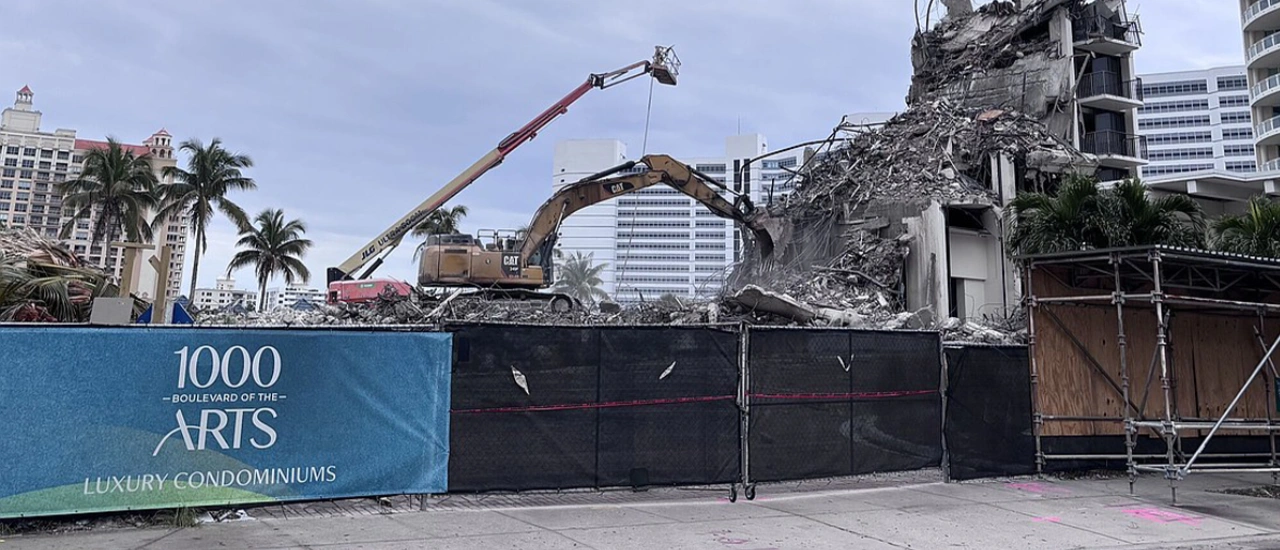 Demolition site with excavators dismantling a concrete building behind fencing