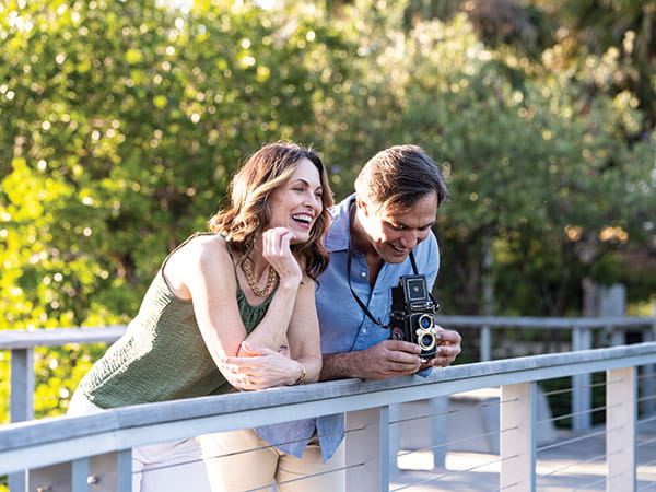 Couple smiling while looking at a camera on an outdoor walkway.