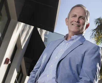 Man in blazer standing outside modern building with palm trees