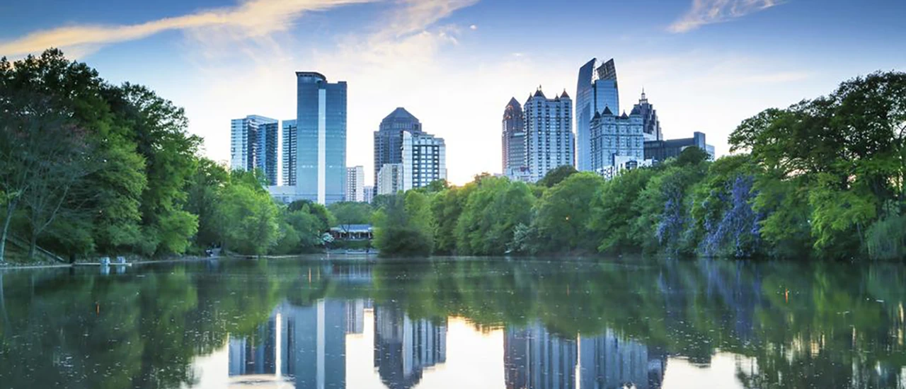 Atlanta skyline reflected in calm lake with trees and sunset sky