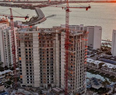 High-rise building under construction with cranes near water at sunset.
