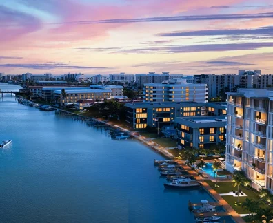 Waterfront condos and marina with boats illuminated at dusk under colorful sunset sky