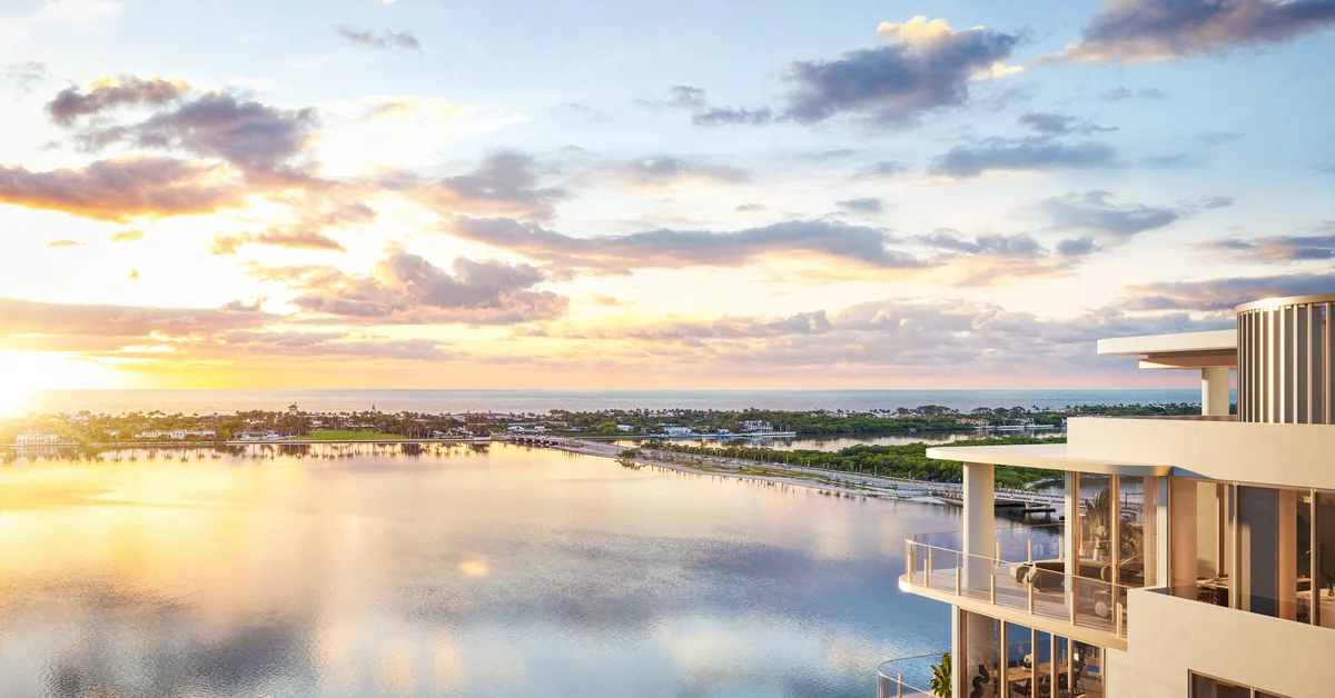 Rendering of a curved building balcony with furnished terraces overlooking a wide waterway at sunset, with a shoreline of trees and estates in the distance and the ocean beyond.